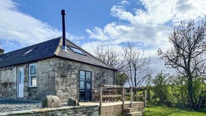 Un bâtiment en pierre doté d’une cheminée, d’une terrasse en bois et d’une zone herbeuse.