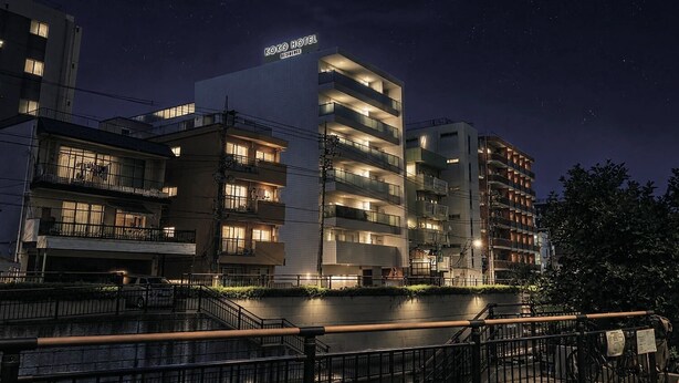 Un hotel de varios pisos con balcones, un cartel que dice 'KOKO HOTEL RESIDENCE' y un ambiente nocturno.