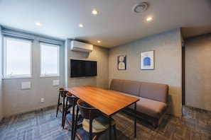 A room with a wooden table, four chairs, a sofa, a flat-screen TV, and two windows with blinds. - KOKO HOTEL Residence Tokyo Oshiage (Sumida-ku)