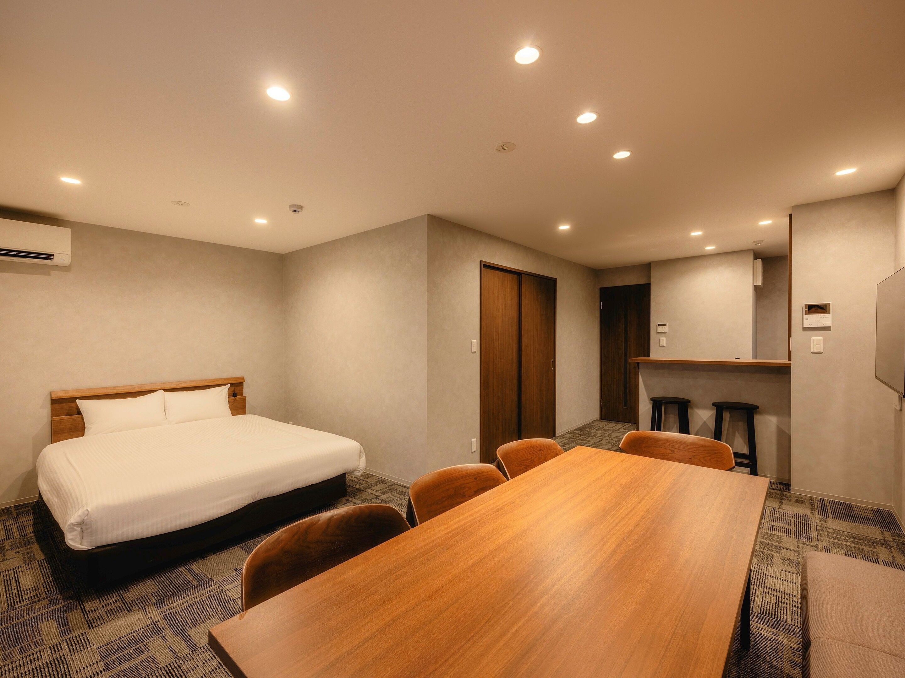 Una habitación de hotel con una cama, una mesita de madera y una pequeña cocina.