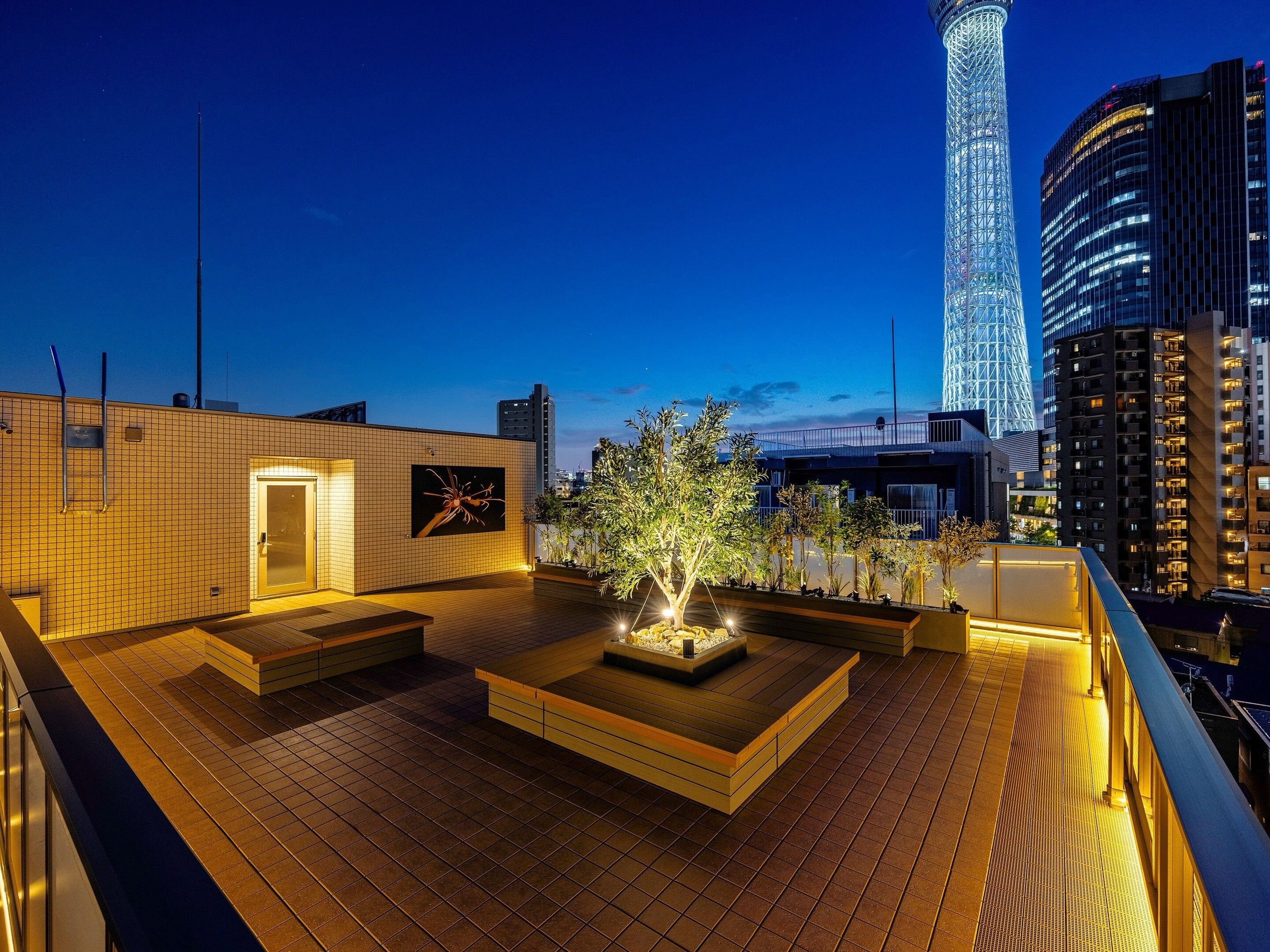 A rooftop terrace with a fire pit, seating areas, and a view of a tall building.