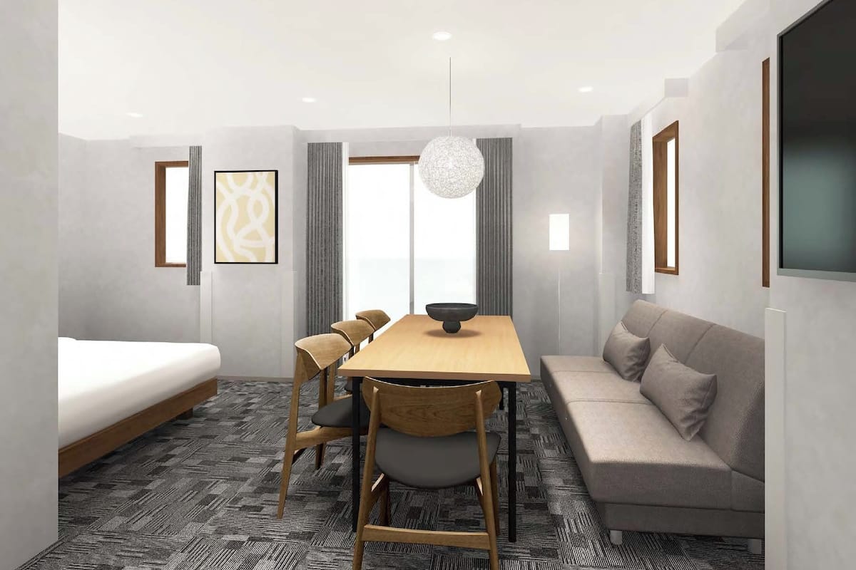 Una habitació d'hotel moderna amb un llit, una taula de dinar amb cadires, un sofà i una finestra gran.