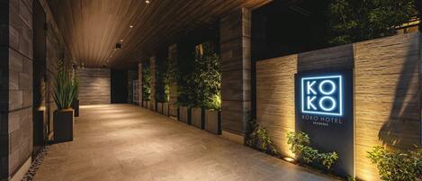 Een gang met een houten plafond, een bord met 'KOKO HOTEL RESIDENCE' en potplanten langs de muren.
