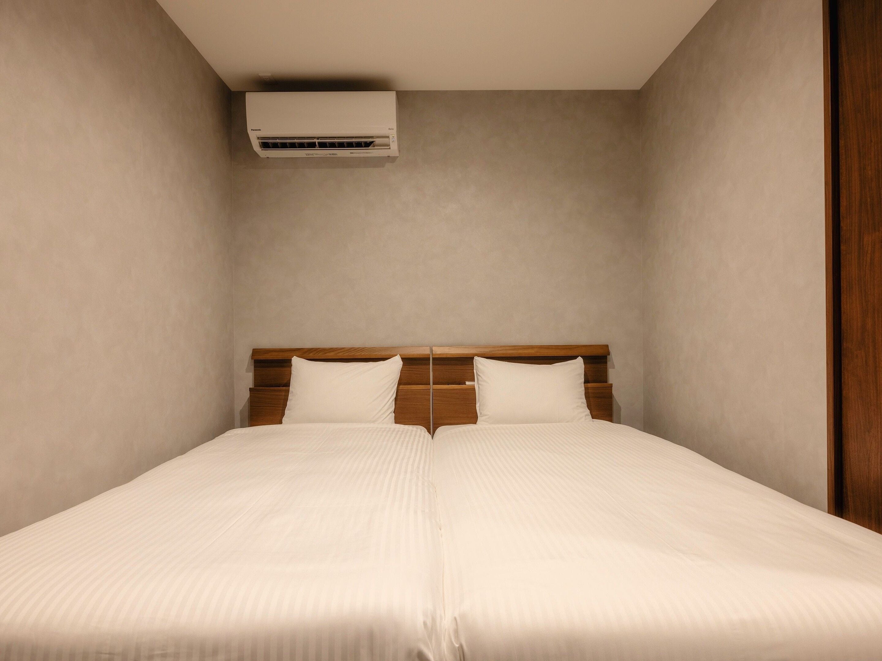 A room with a bed, a wooden headboard, and an air conditioning unit mounted on the wall.