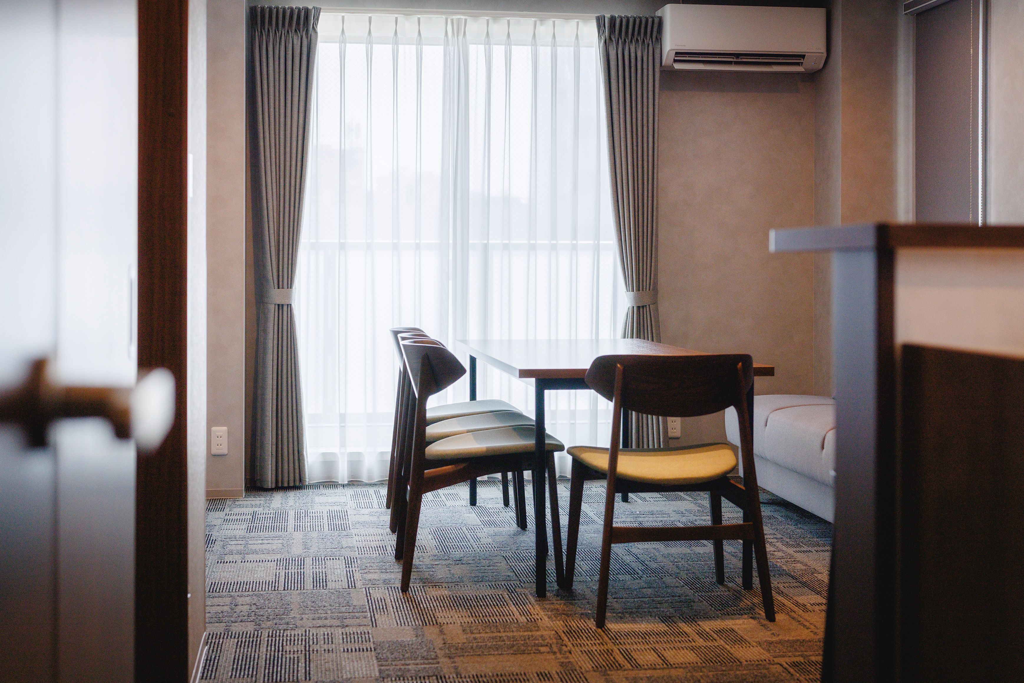Habitación de hotel con zona de comedor, sofá y alfombra estampada.
