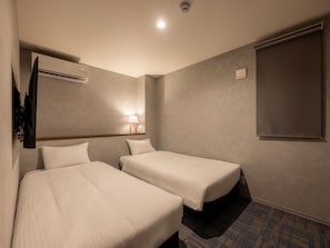 A hotel room with two beds, a flat-screen TV mounted on the wall, an air conditioning unit, a bedside lamp, and a window with a blind. - KOKO HOTEL Residence Tokyo Oshiage (Sumida-ku)
