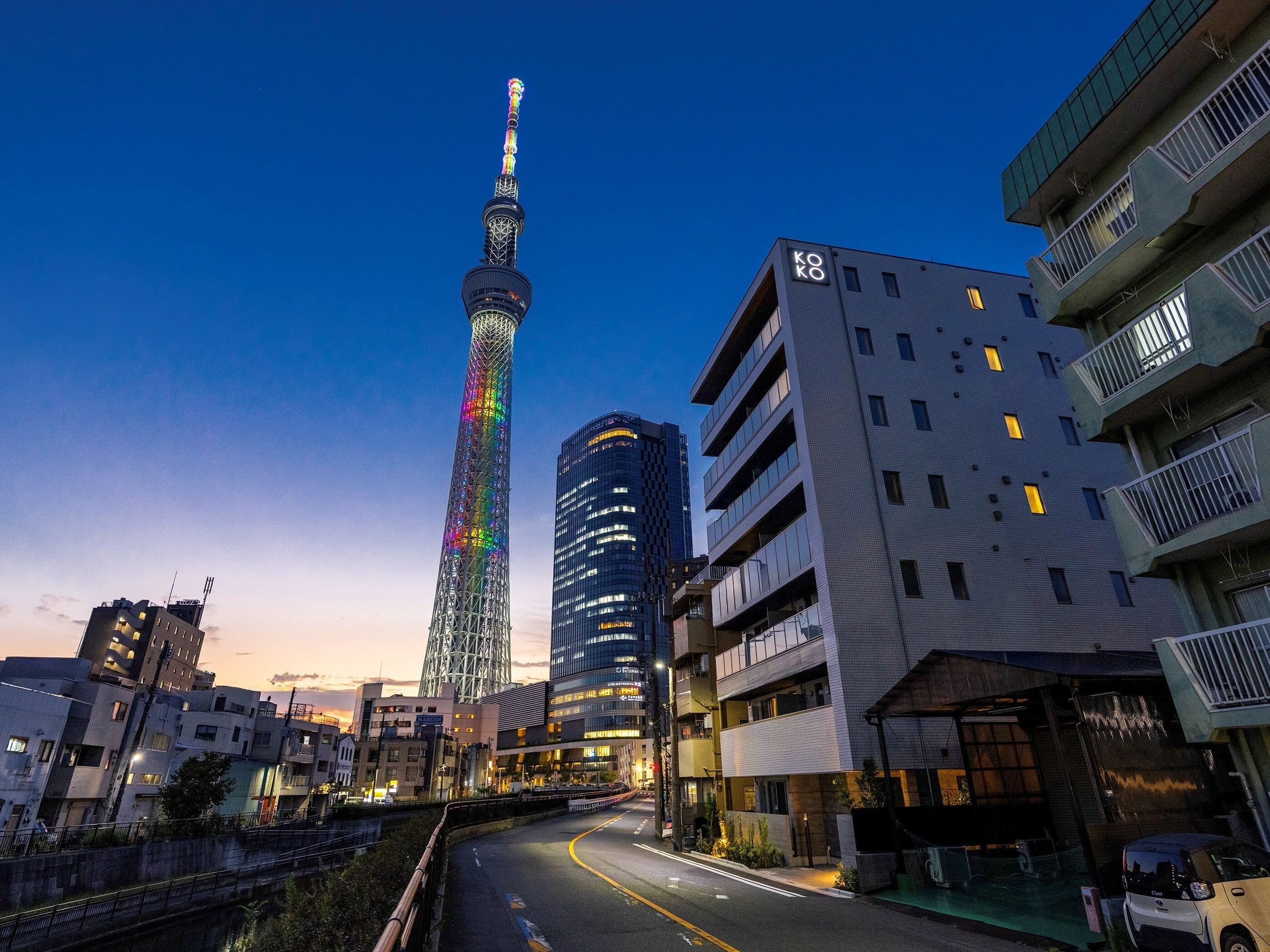 A cityscape with modern buildings, a prominent tower with colorful lights, and a clear sky.