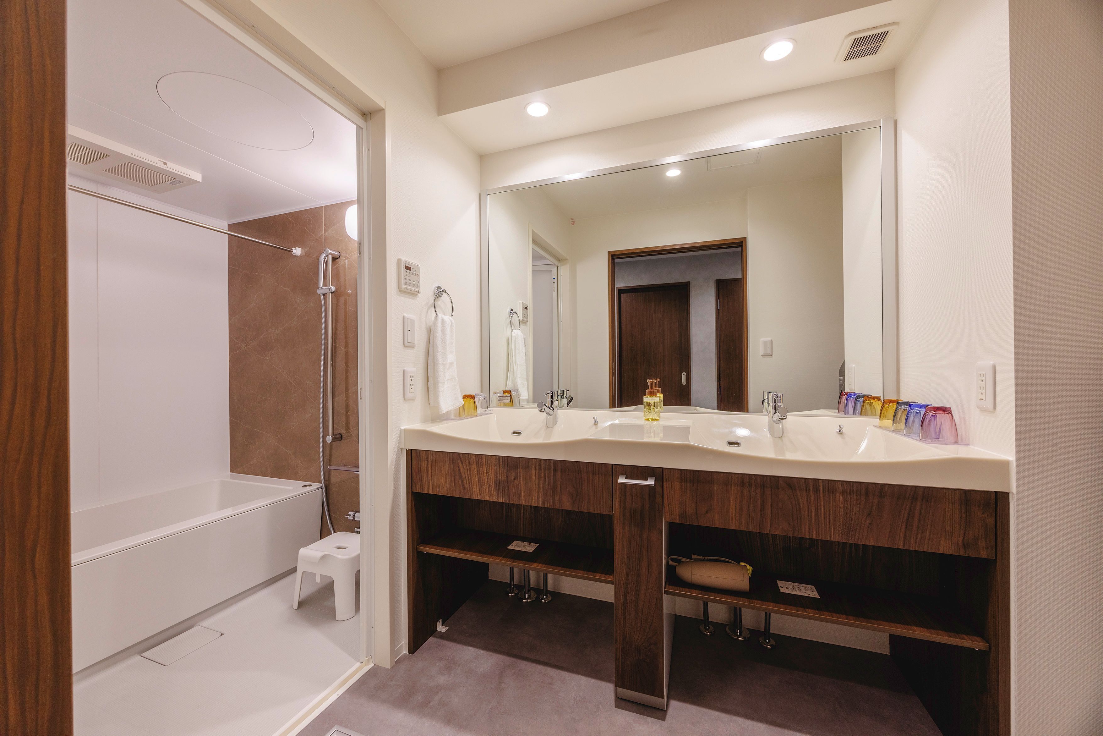 A modern bathroom with a walk-in shower, a double vanity with a large mirror, and a wooden vanity with a towel rack.
