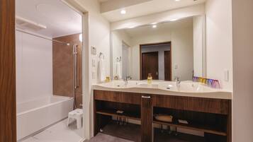 A modern bathroom with a walk-in shower, a double vanity with a large mirror, and a wooden vanity with a towel rack.