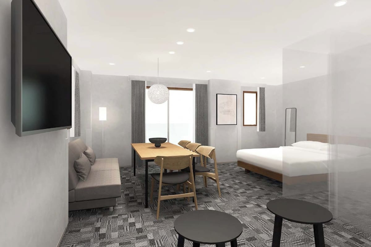 Habitació d'hotel moderna amb televisió de pantalla plana, un sofà, una taula de menjador amb cadires, un llit i una taula petita.