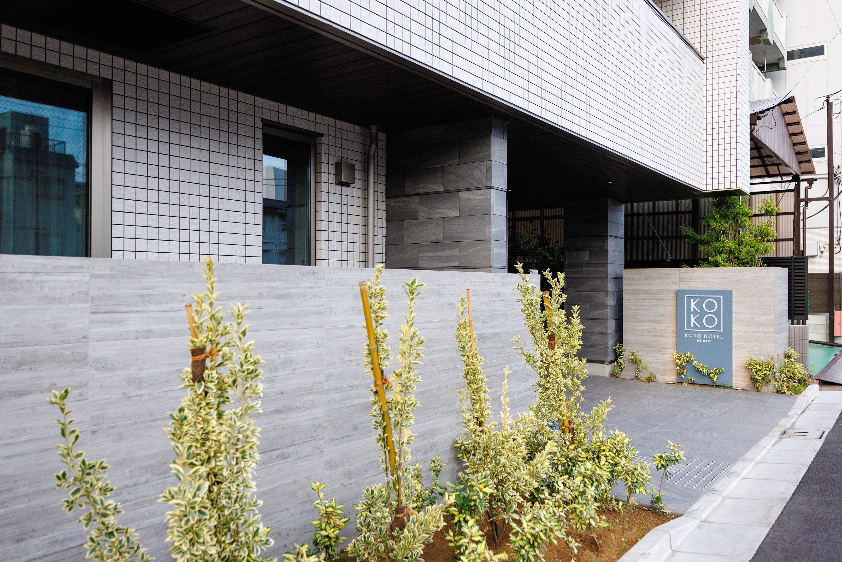 A modern building with a tiled facade, a concrete wall, and a sign for the Kokobo Hotel.