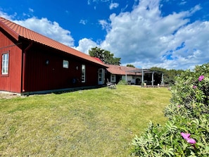 Un bâtiment rouge doté d’un patio couvert, d’une pelouse et d’un jardin agrémenté de fleurs roses.