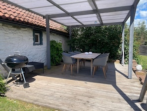 Un patio couvert avec une table et des chaises, un barbecue et une terrasse en bois.