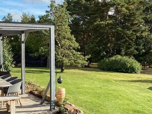 A wooden deck with a pergola, a table with chairs, and a large tree in the background. - 4 Star Holiday Home in Farjestaden (Farjestaden)