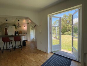 A kitchen with wooden flooring, a bar area with stools, and a large sliding glass door leading to a garden. - 4 Star Holiday Home in Farjestaden (Farjestaden)
