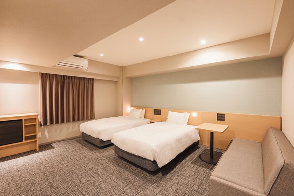 Une chambre d’hôtel avec deux lits, un bureau, un canapé, un appareil de climatisation et un rideau.
