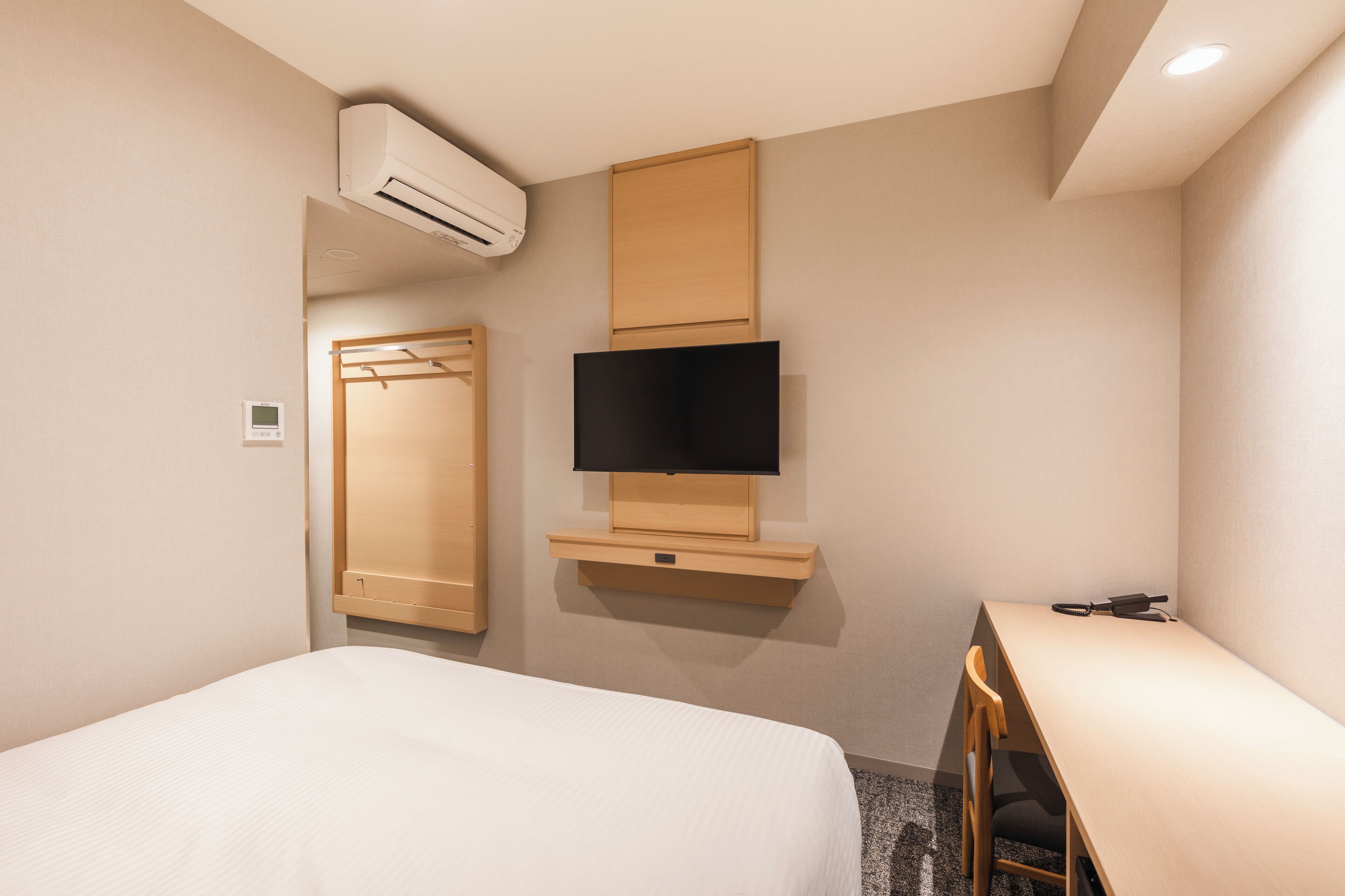 Habitación de hotel con cama, televisor montado en un panel de madera, armario y unidad de aire acondicionado.