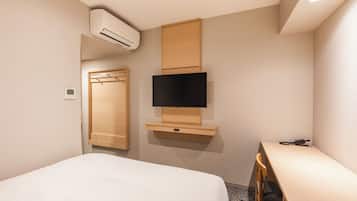 Habitación de hotel con cama, televisor montado en un panel de madera, armario y unidad de aire acondicionado.