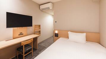 A hotel room with a bed, a desk with a chair, a television, and an air conditioning unit.