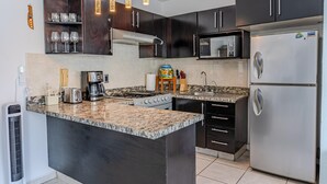 Eine moderne Küche mit dunklen Schränken, einer Arbeitsplatte aus Granit, einem Edelstahlkühlschrank und einer Mikrowelle.