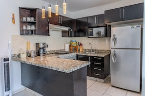 A modern kitchen with dark cabinets, a granite countertop, a stainless steel refrigerator, and a microwave. - Bright & Comfortable Condo in Heart of Versalles! 2BD Condo for rent in Versalle (Puerto Vallarta)