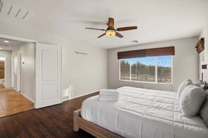 Quarto com cama, ventilador de teto, janela com persianas e porta que dá para outro cômodo.