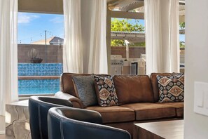 A brown leather sofa with patterned cushions, a dining table, and a view of a swimming pool and outdoor area. - Spacious 5BR Gilbert Home w Pool for Getaway for Family (Gilbert)