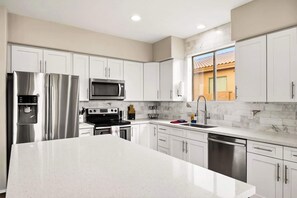 A modern kitchen with white cabinets, stainless steel appliances, a marble backsplash, and a large island. - Spacious 5BR Gilbert Home w Pool for Getaway for Family (Gilbert)