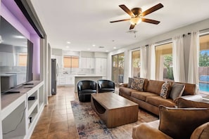 A modern living room with a sofa, coffee table, and chairs, a kitchen with white cabinets, and a ceiling fan. - Spacious 5BR Gilbert Home w Pool for Getaway for Family (Gilbert)
