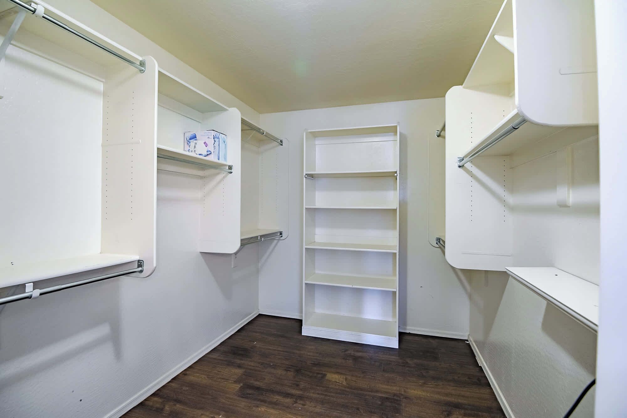 A narrow hallway with white walls and wooden flooring, featuring built-in shelving units on both sides.