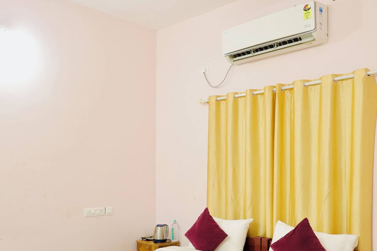 Un lit simple avec un cadre en bois, un ventilateur de plafond, un appareil de climatisation et des rideaux jaunes.