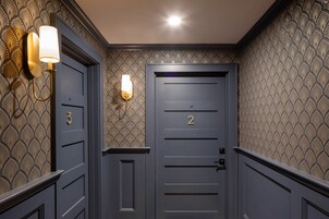Un pasillo con dos puertas, una con el número 3 y la otra con el número 2, y una lámpara en la pared.