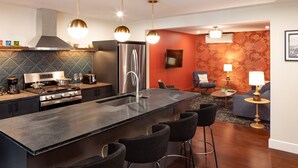 A modern kitchen with a central island, bar stools, a refrigerator, and a dining area with a sofa and a table. - Shelburne Springs Hotel (Shelburne)