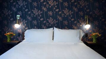 A bed with white linens, two bedside tables with lamps, and a floral wallpaper pattern.