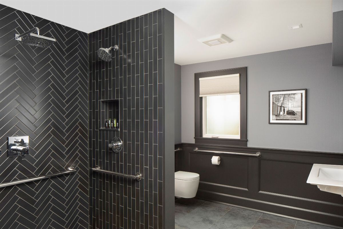 Une salle de bain moderne avec un carrelage disposé en motif «chevrons», une douche, des toilettes, un lavabo et une fenêtre.