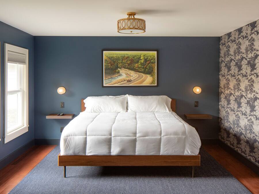 A bedroom with a bed, two bedside lamps, a painting, and a patterned wallpaper.