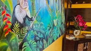 Una habitación con un gran mural de un mono sosteniendo una espada, una planta en maceta y una mesita con una lámpara y libros.