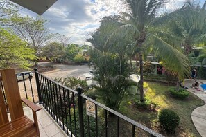 A balcony with a view of a garden, a pool, and a road. - Colorful Tropical Studio | King Bed | Walk 2 Beach (Coco)