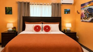 Una cama con una manta marrón, dos almohadones florales rojos y un cabecero de madera.
