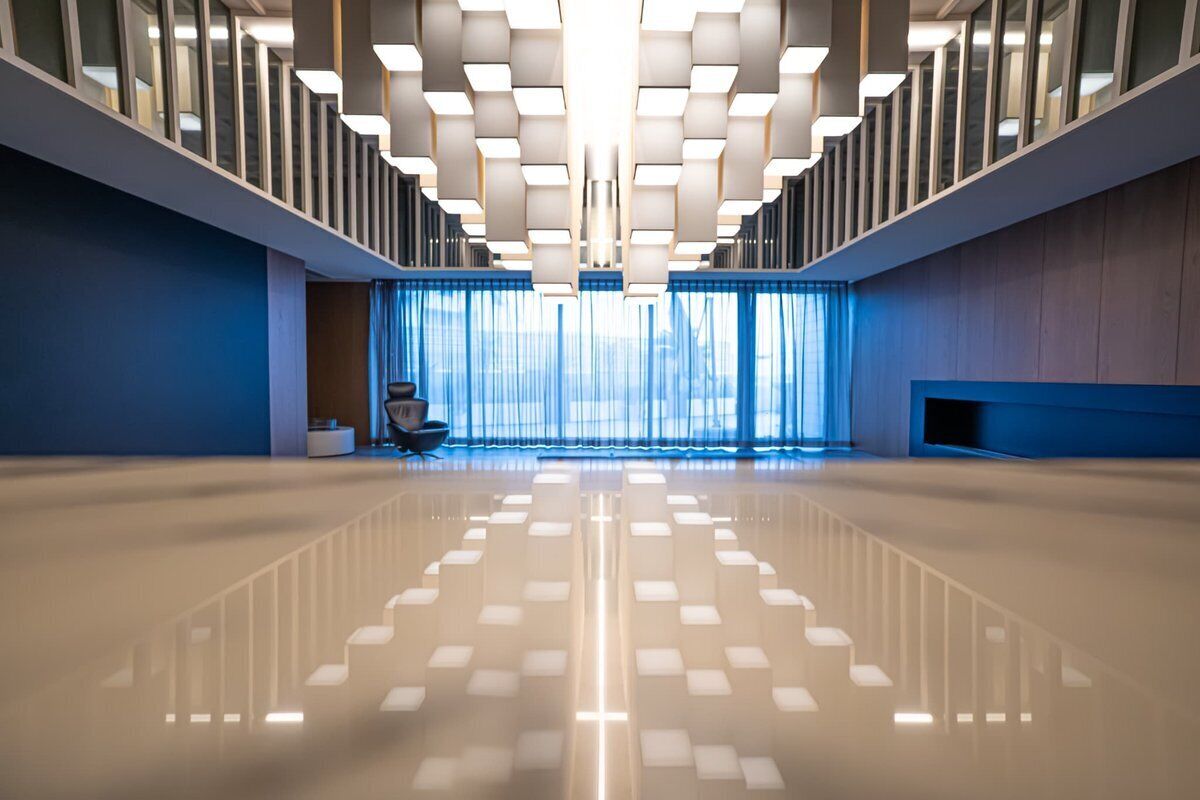 A spacious lobby with a reflective floor, a staircase with a unique geometric design, and a seating area with a modern chair.