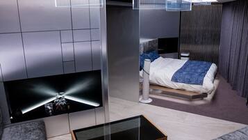 A modern hotel room with a bed, a TV mounted on the wall, a glass coffee table, and a sofa.