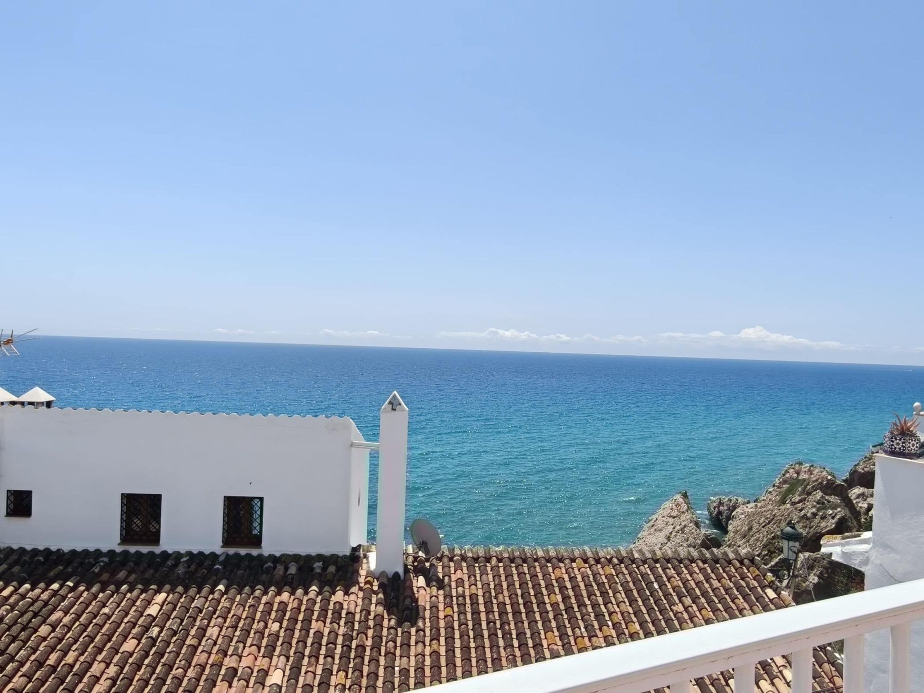 A coastal building with a tiled roof, a white facade, and a view of the sea.