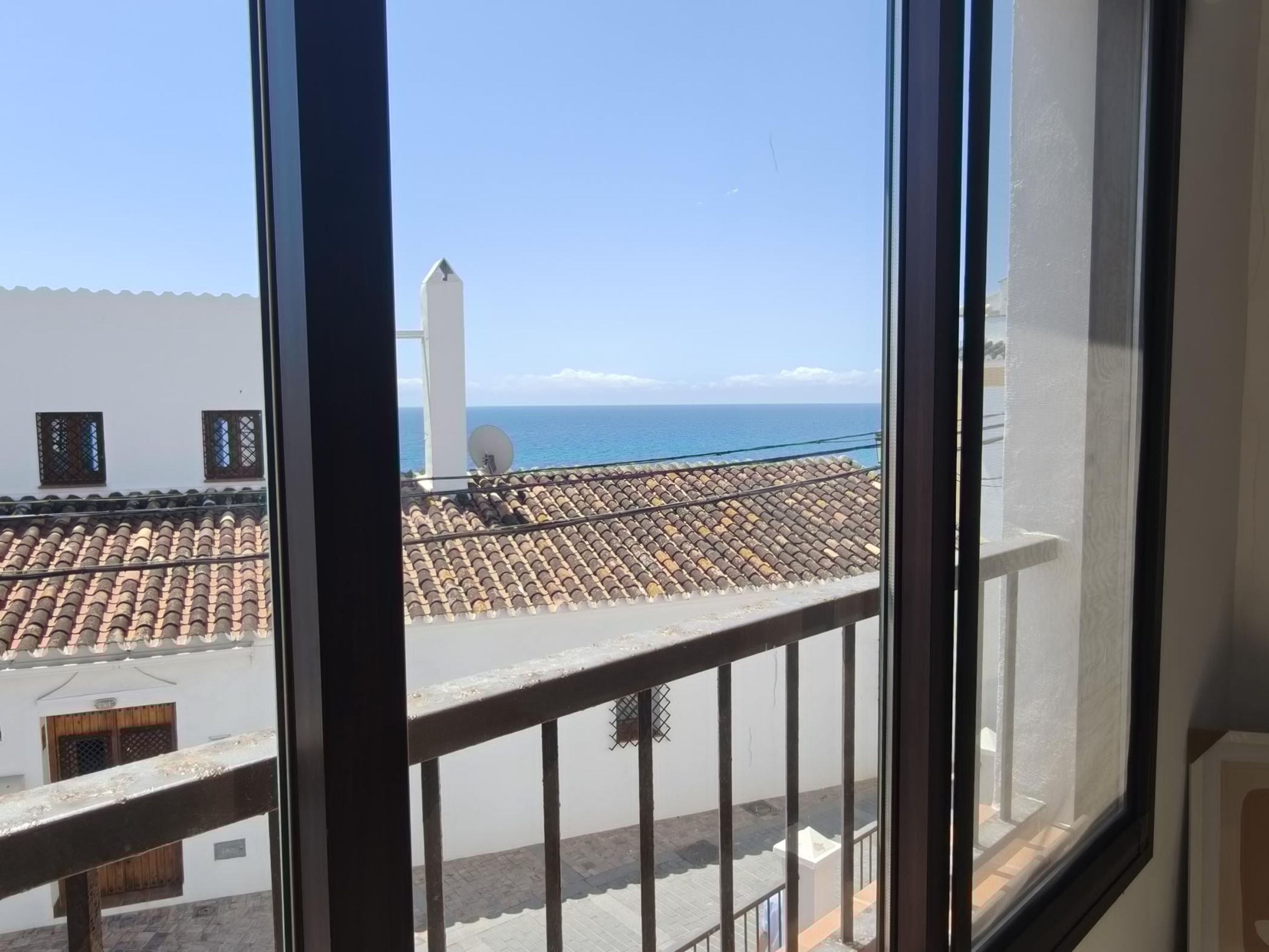 A view from a window overlooking a tiled rooftop with a white building and a white tower in the distance.