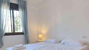 Ett hotellrum med en säng, två kuddar, ett nattduksbord med en lampa och ett fönster med gardiner.