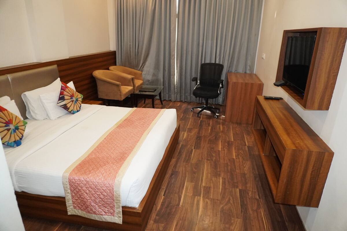 Habitación de hotel con cama, escritorio, silla, televisor y ventana con cortinas.