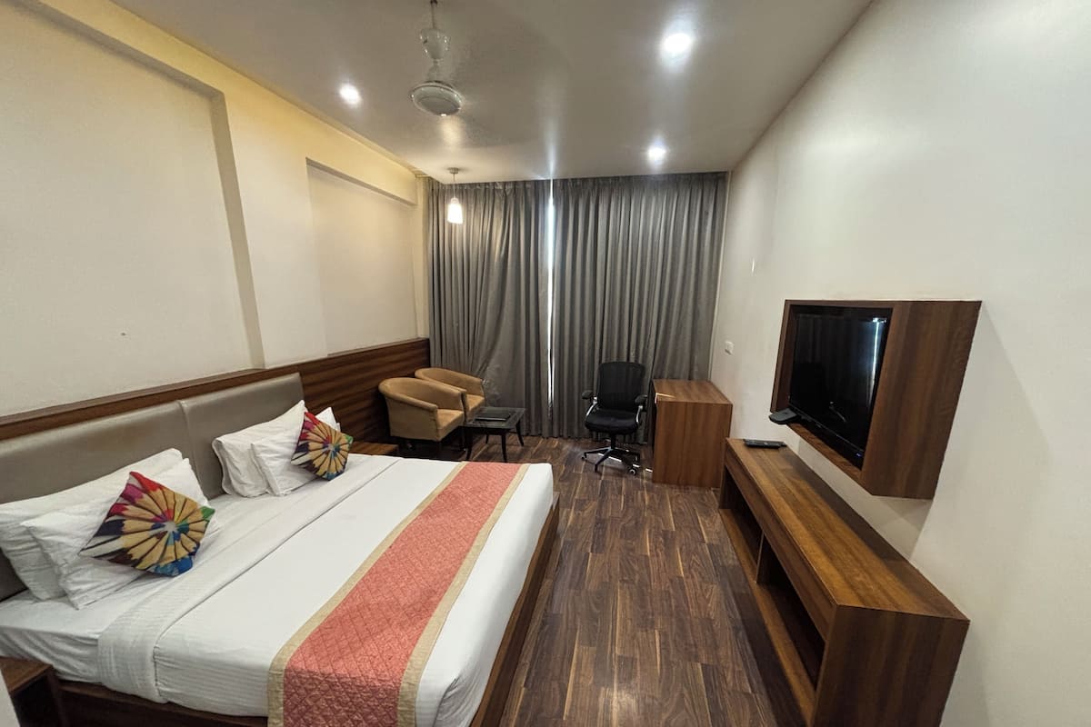 Habitación de hotel con cama, escritorio, silla, televisor y ventana con cortinas.