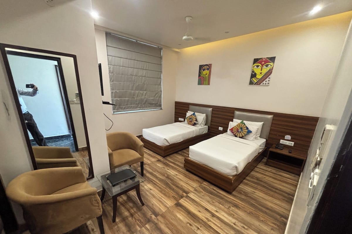 Habitación de hotel con dos camas, una silla, una mesita y obras de arte en las paredes.