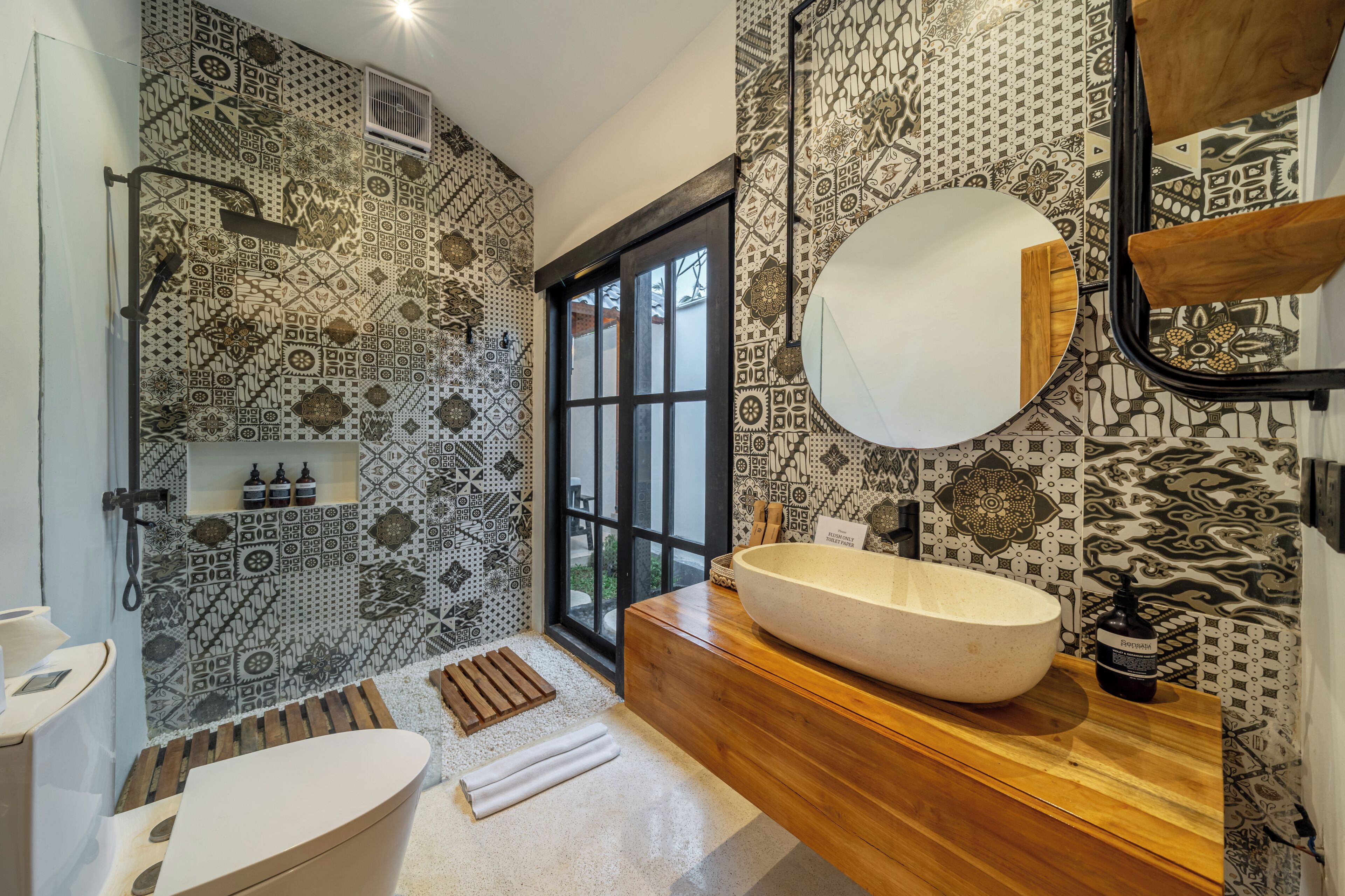 A modern bathroom with patterned tiles, a large mirror, a wooden vanity, and a window.