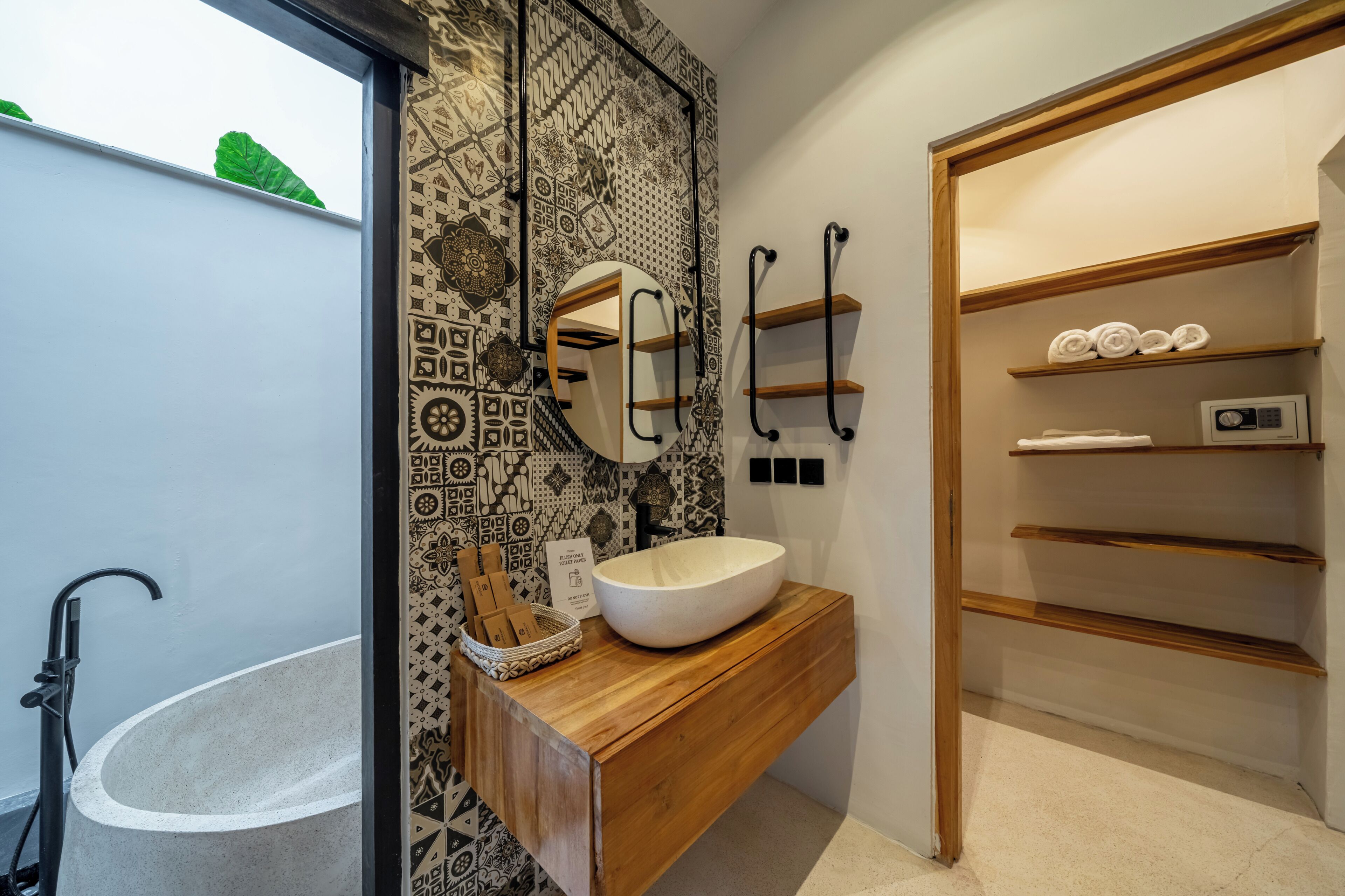 A modern bathroom with a freestanding bathtub, a wooden vanity with a large sink, a mirror, and patterned wall tiles.