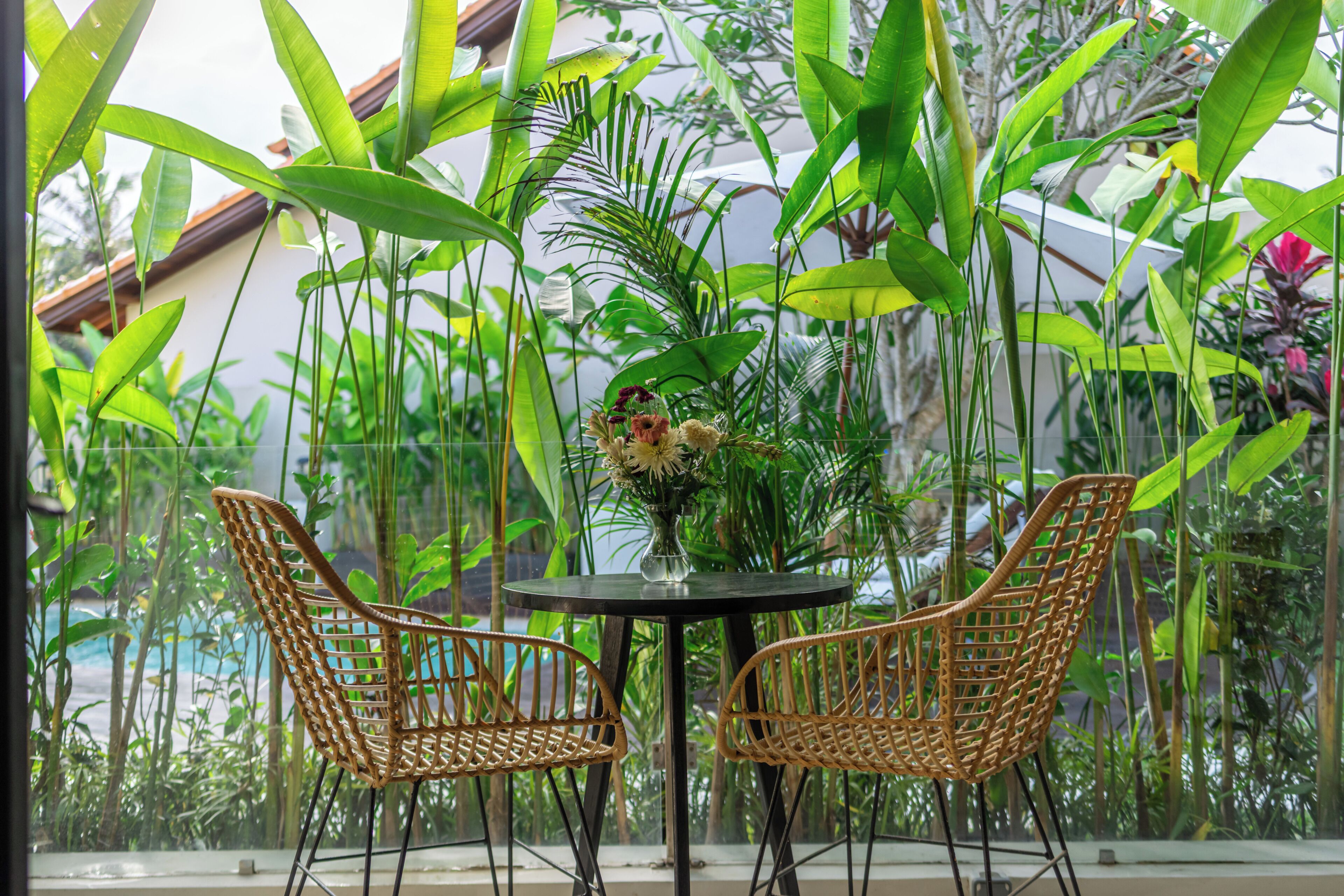 Un balcon avec des fauteuils en osier, une table et un vase de fleurs.